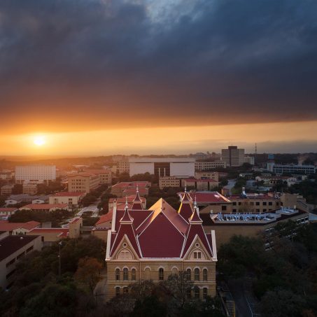 The setting sun blazes through a gap in the heavy clouds behind Old Main and Texas State University.